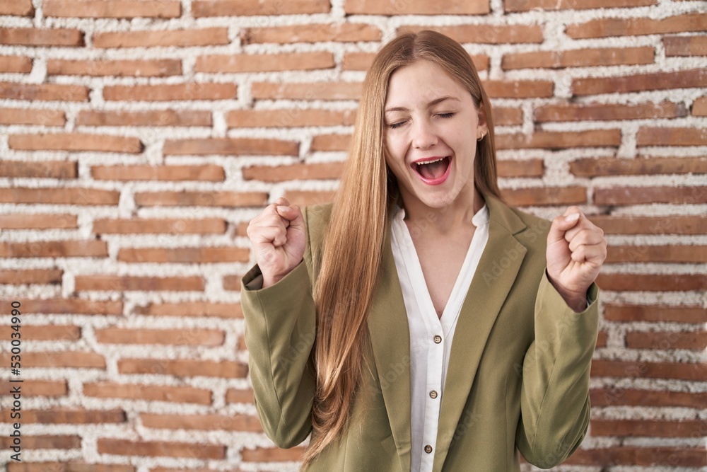 Young caucasian woman standing over bricks wall background excited for success with arms raised and eyes closed celebrating victory smiling. winner concept. Young caucasian woman standing over bricks wall background excited for success with arms raised and eyes closed celebrating victory smiling. winner concept.