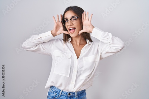 Canvastavla Young brunette woman wearing glasses smiling cheerful playing peek a boo with hands showing face