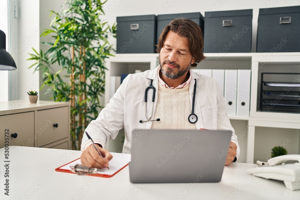 Middle age man doctor drinking coffee writing on document at clinic Middle age man doctor drinking coffee writing on document at clinic