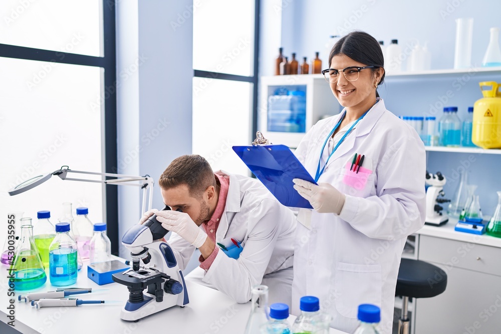 Man and woman wearing scientists uniform using microscope at laboratory Man and woman wearing scientists uniform using microscope at laboratory