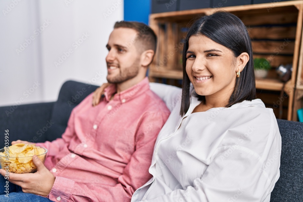 Man and woman couple eating chips potatoes sitting on sofa at home Man and woman couple eating chips potatoes sitting on sofa at home