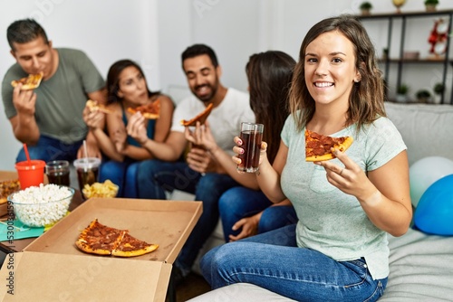 Group of young hispanic friends smiling happy eating italian pizza sitting on the sofa at home.