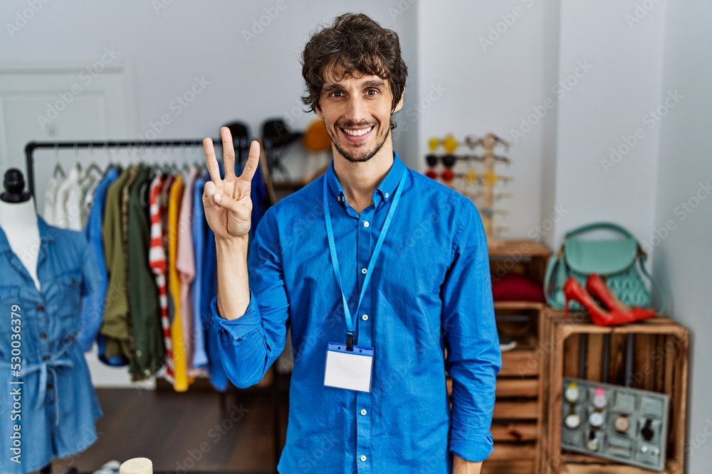 Young hispanic man working as manager at retail boutique showing and pointing up with fingers number three while smiling confident and happy. Young hispanic man working as manager at retail boutique showing and pointing up with fingers number three while smiling confident and happy.