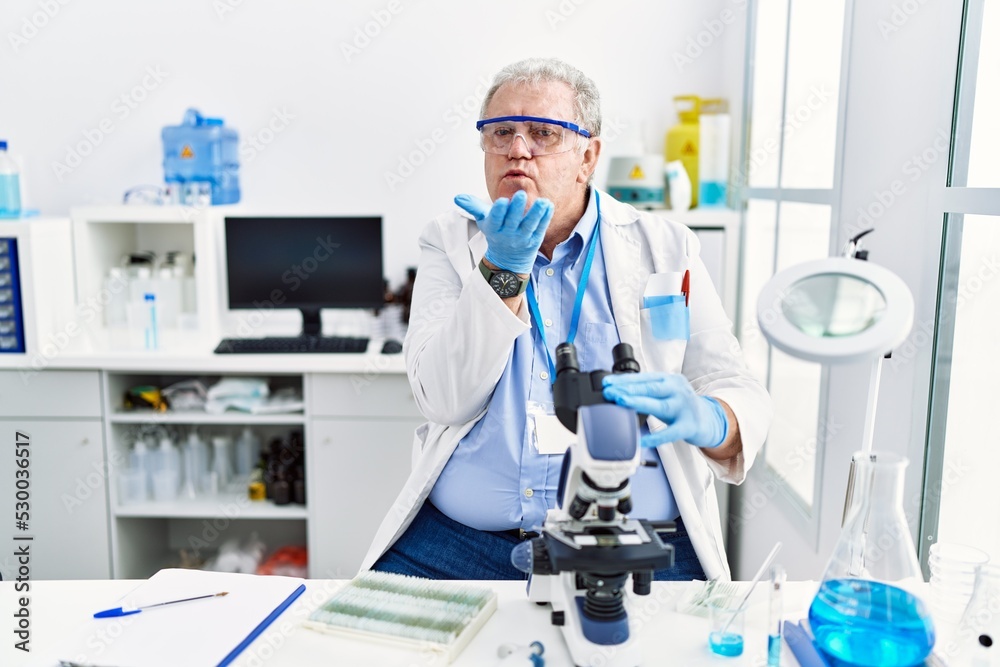 Senior caucasian man working at scientist laboratory looking at the camera blowing a kiss with hand on air being lovely and sexy. love expression. Senior caucasian man working at scientist laboratory looking at the camera blowing a kiss with hand on air being lovely and sexy. love expression.
