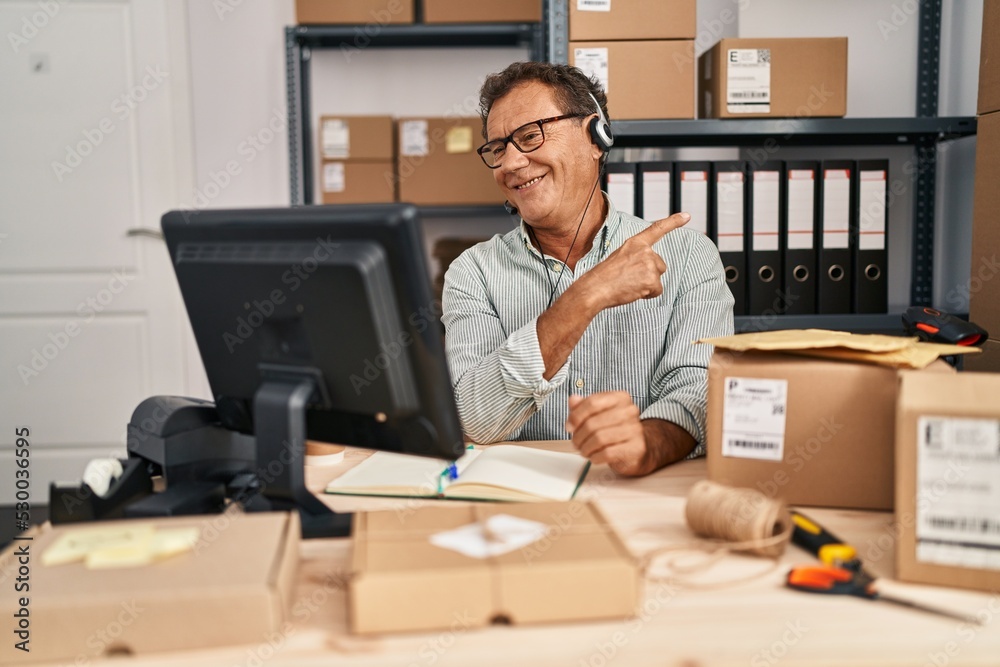 Senior man working at small business ecommerce wearing headset smiling cheerful pointing with hand and finger up to the side Senior man working at small business ecommerce wearing headset smiling cheerful pointing with hand and finger up to the side