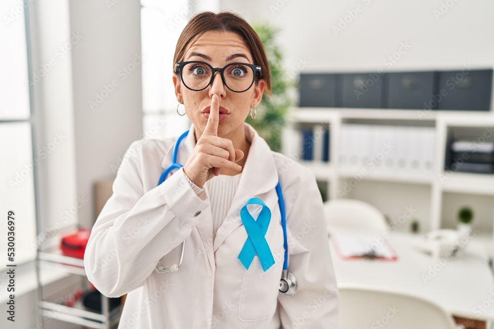 Young brunette doctor woman wearing stethoscope at the clinic asking to be quiet with finger on lips. silence and secret concept.