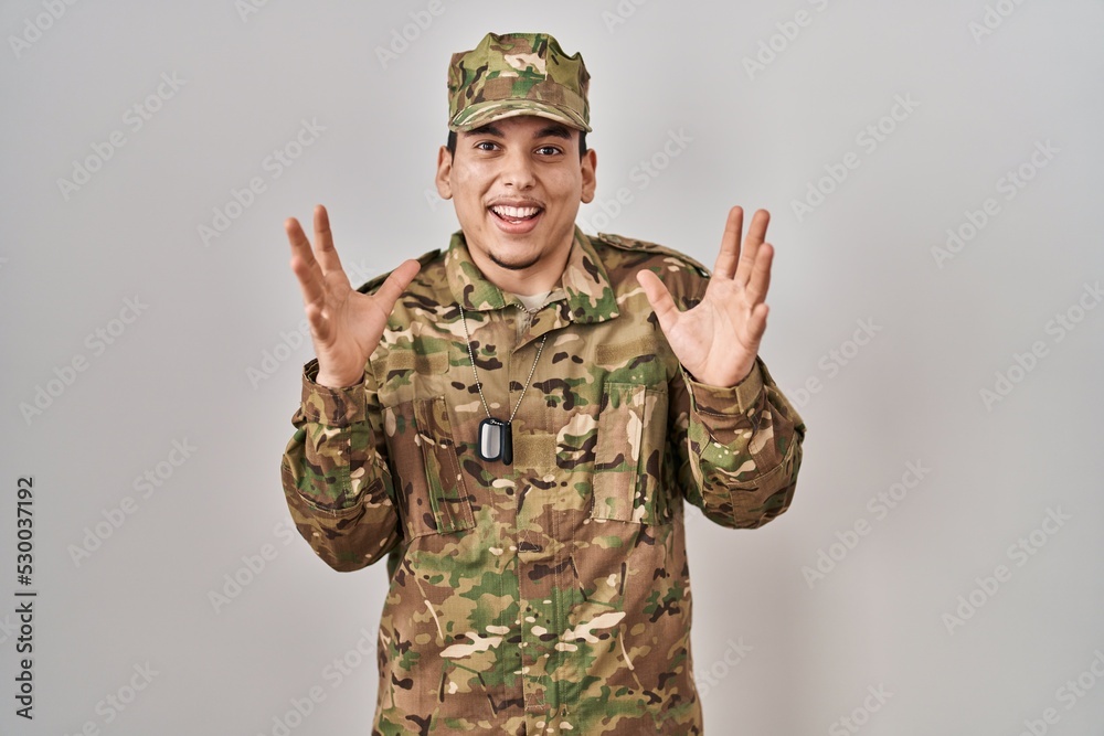 Young arab man wearing camouflage army uniform celebrating crazy and amazed for success with arms raised and open eyes screaming excited. winner concept Young arab man wearing camouflage army uniform celebrating crazy and amazed for success with arms raised and open eyes screaming excited. winner concept