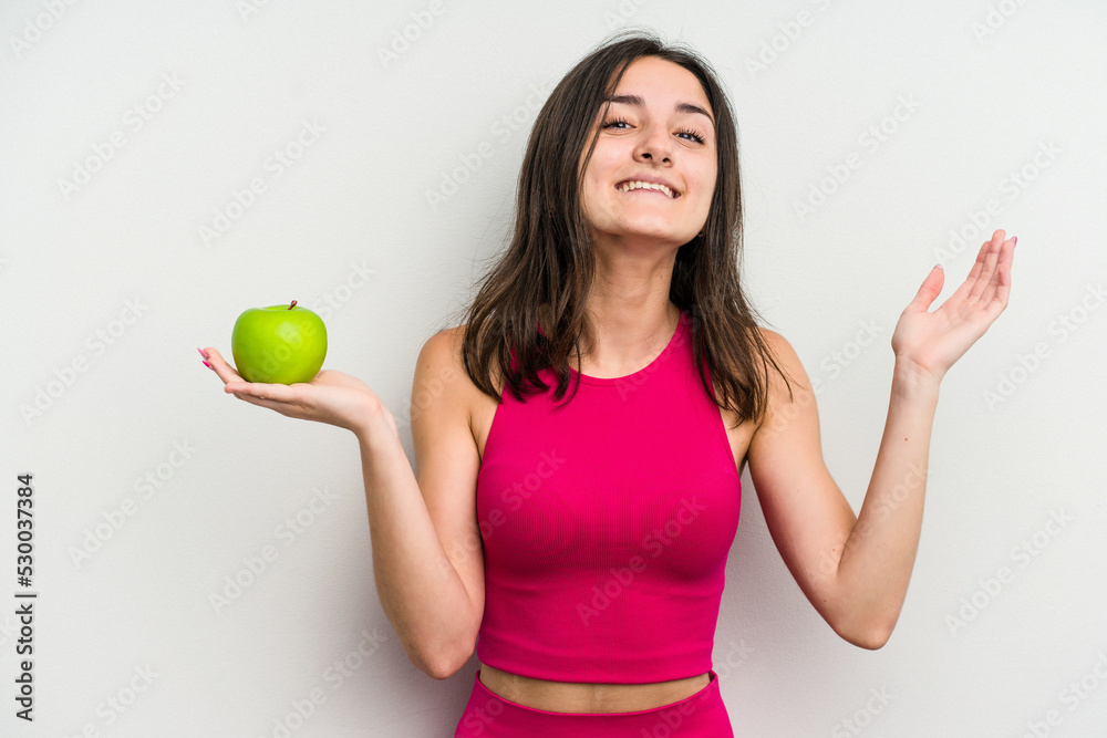 Young caucasian woman holding an apple isolated on white background receiving a pleasant surprise, excited and raising hands. Young caucasian woman holding an apple isolated on white background receiving a pleasant surprise, excited and raising hands.
