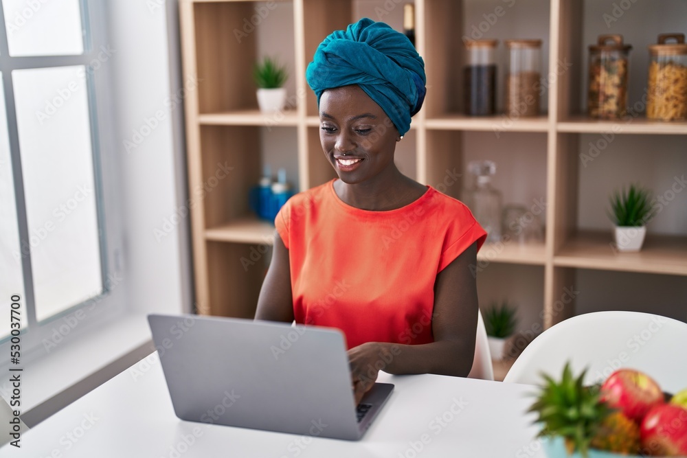 Young african american woman using laptop sitting on table at home Young african american woman using laptop sitting on table at home