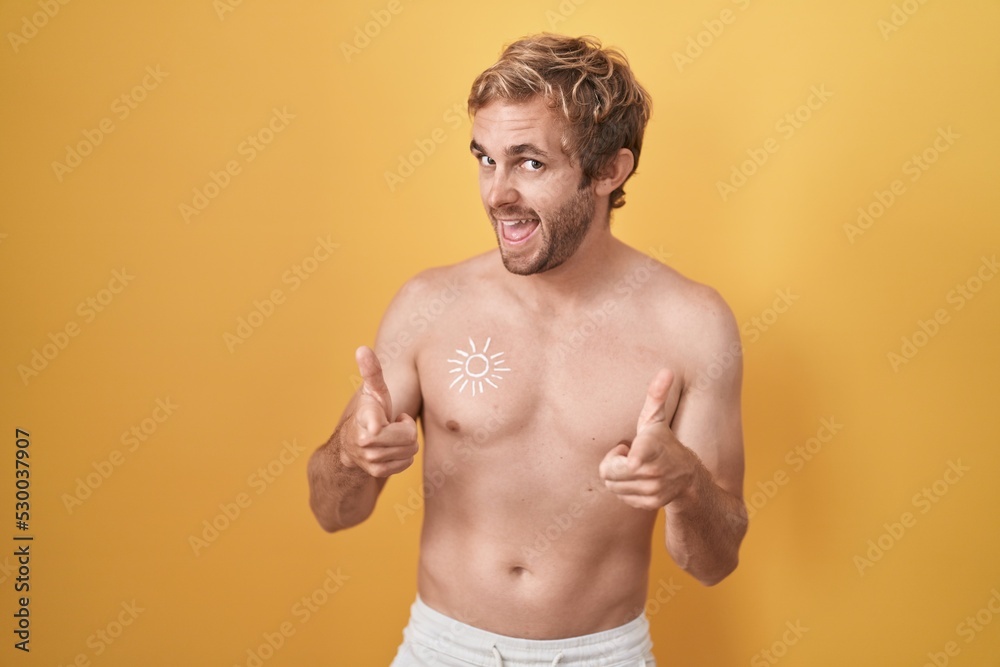 Fototapeta premium Caucasian man standing shirtless wearing sun screen pointing fingers to camera with happy and funny face. good energy and vibes.