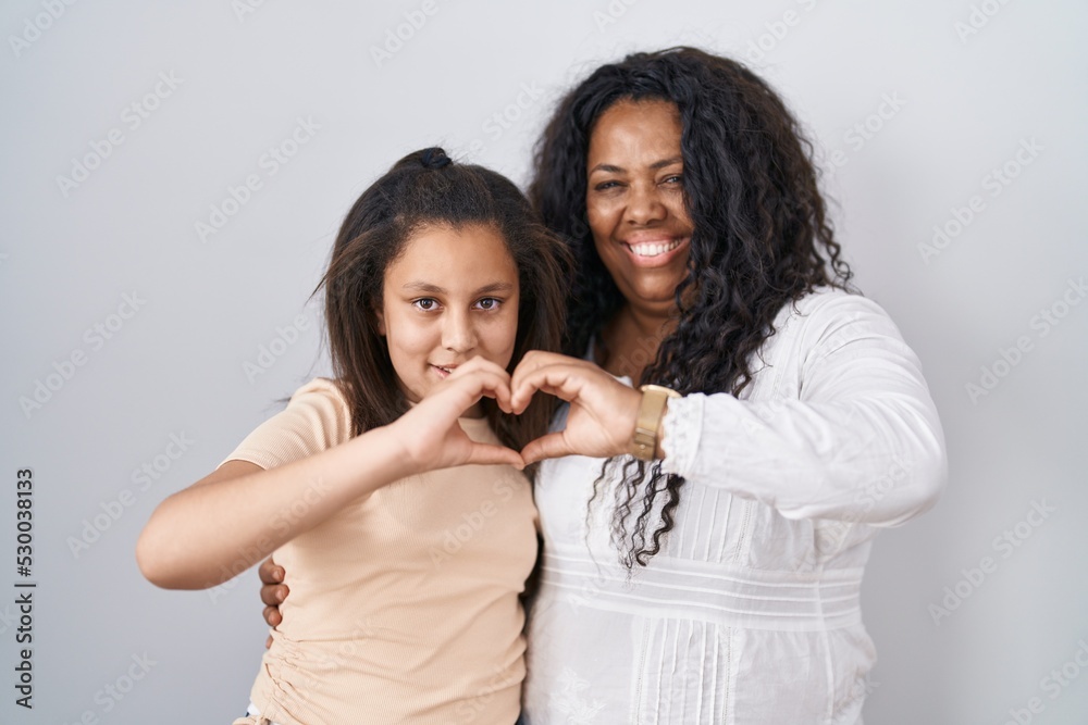 Mother and young daughter standing over white background smiling in love doing heart symbol shape with hands. romantic concept.