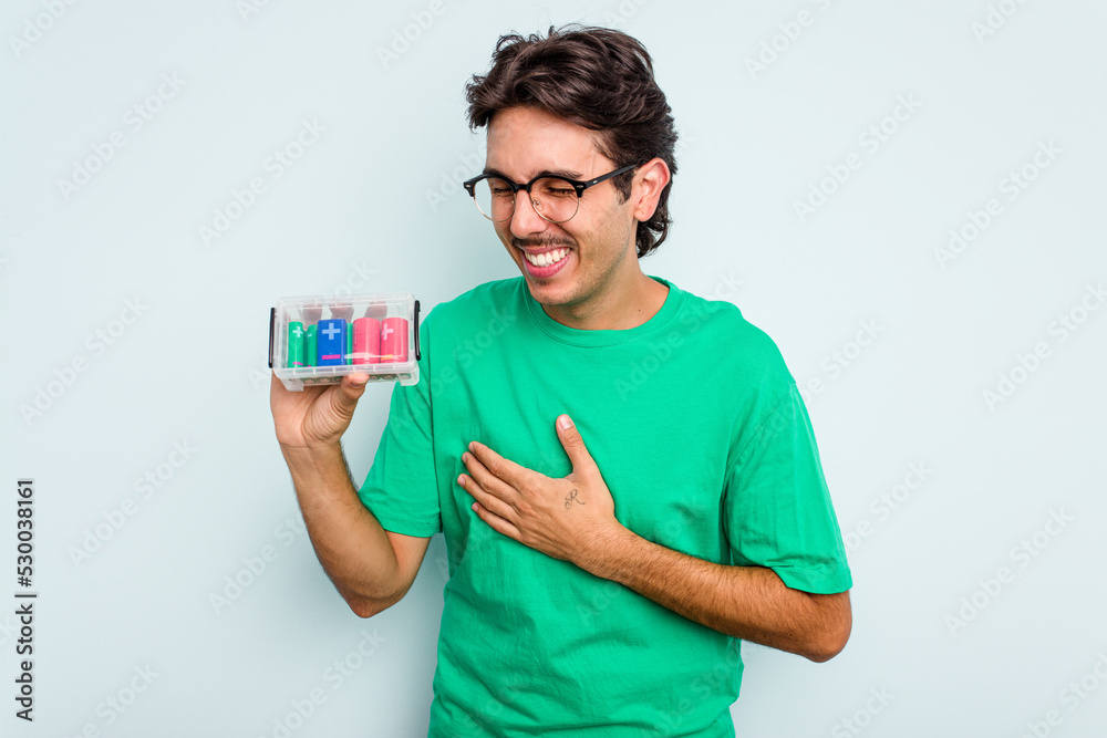 Young hispanic man holding battery box isolated on white background laughing and having fun. Young hispanic man holding battery box isolated on white background laughing and having fun.