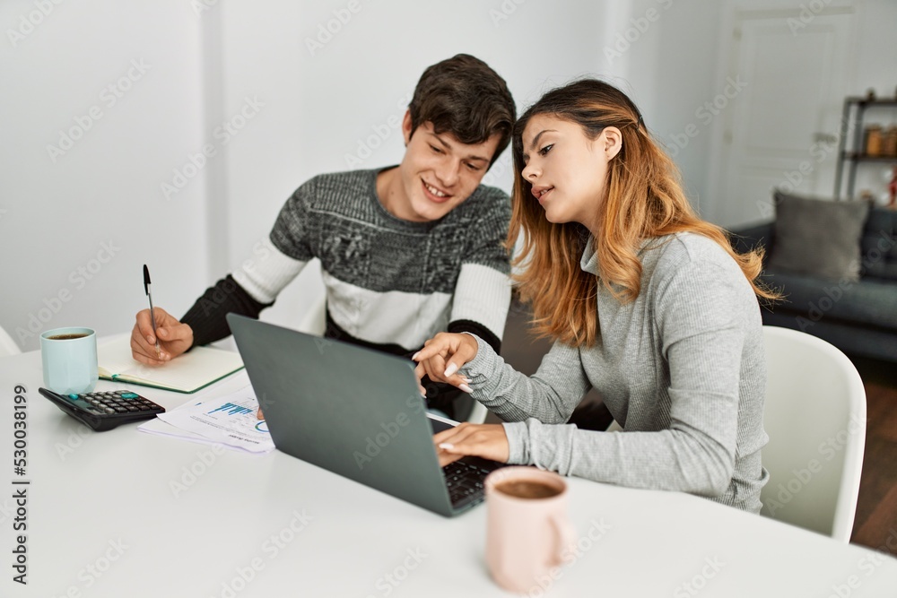 Young couple smiling happy working using laptop sitting on the table at home. Young couple smiling happy working using laptop sitting on the table at home.