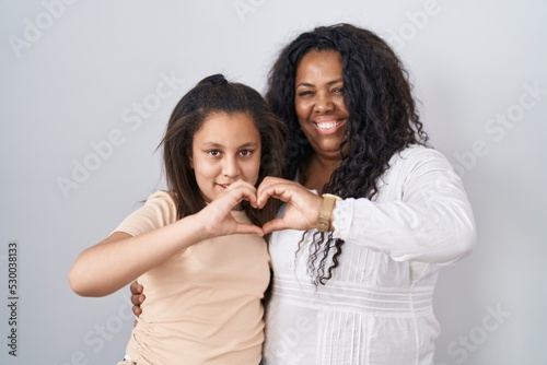 Mother and young daughter standing over white background smiling in love doing heart symbol shape with hands. romantic concept.