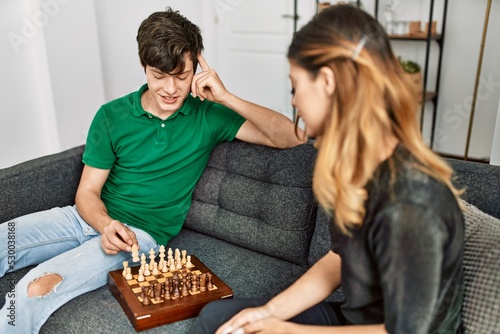 Young caucasian couple smiling happy playing chess game sitting on the sofa at home.