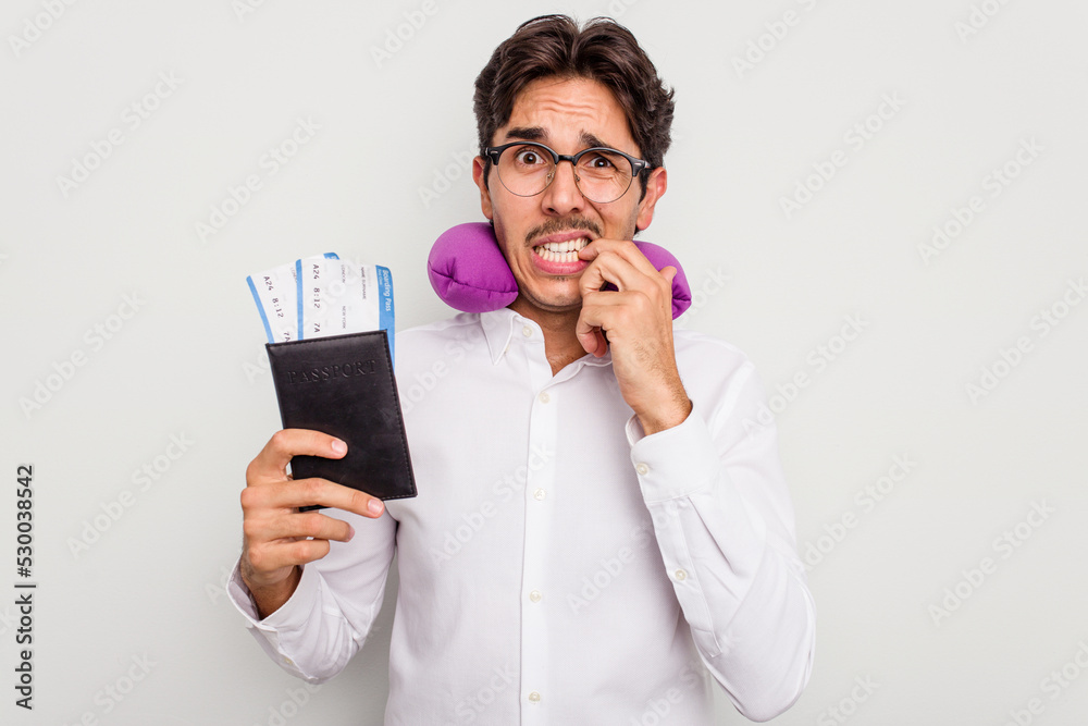 Young hispanic man with inflatable travel pillow holding passport isolated on white background biting fingernails, nervous and very anxious. Young hispanic man with inflatable travel pillow holding passport isolated on white background biting fingernails, nervous and very anxious.