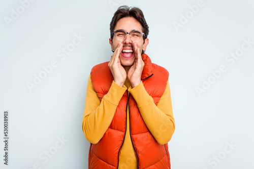 Young hispanic man isolated on blue background saying a gossip, pointing to side reporting something.