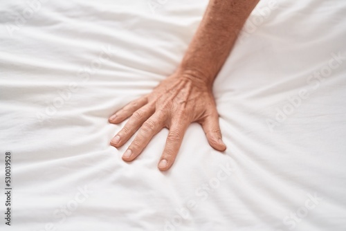 Middle age man touching bed sheet at bedroom