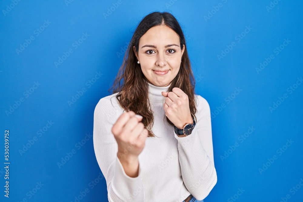 Young hispanic woman standing over blue background ready to fight with fist defense gesture, angry and upset face, afraid of problem Young hispanic woman standing over blue background ready to fight with fist defense gesture, angry and upset face, afraid of problem