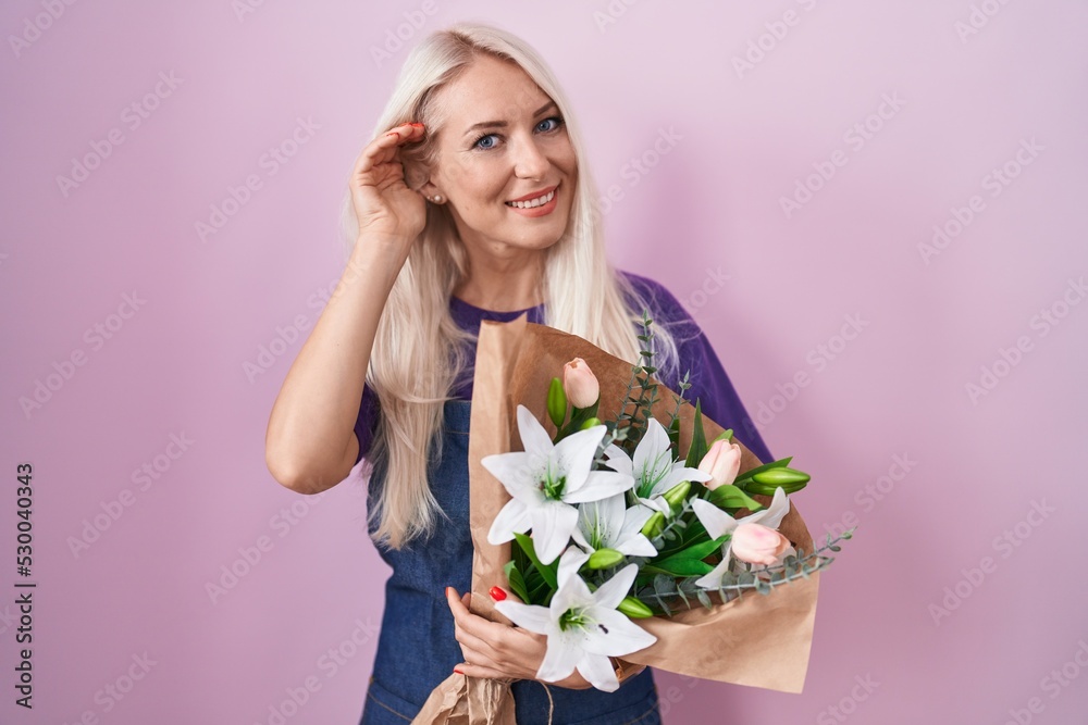 Caucasian woman holding bouquet of white flowers smiling with hand over ear listening an hearing to rumor or gossip. deafness concept.