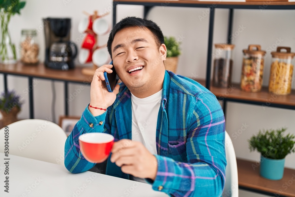 Young chinese man drinking coffee and talking on the smartphone at home Young chinese man drinking coffee and talking on the smartphone at home