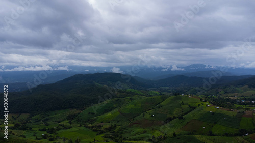 Fototapeta Naklejka Na Ścianę i Meble -  Aerial view of green wave fields with mountains and cloudy sky in rainy season. Beautiful green area of young rice fields or agricultural land in northern Thailand. Natural landscape background.
