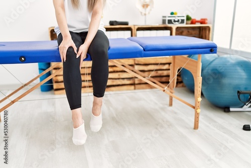 Young chinese woman with pain on knee sitting on board at clinic