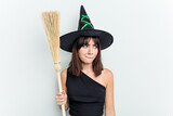 Young caucasian woman dressed as a witch holding a broom isolated on blue background confused, feels doubtful and unsure.
