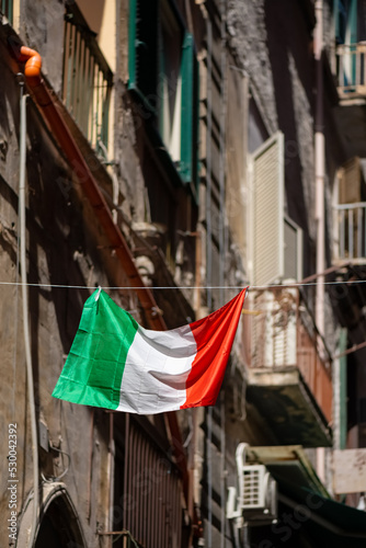 Italian flag in national colors green, white and red haging in a narrow street of old town of Naples. Tricolore blown by wind with facades of old houses with small balconys blurred in the background. © ON-Photography