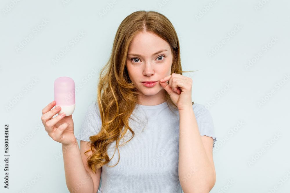 Young caucasian woman holding deodorant isolated on blue background with fingers on lips keeping a secret. Young caucasian woman holding deodorant isolated on blue background with fingers on lips keeping a secret.