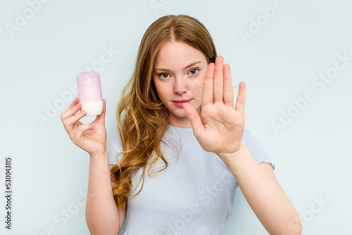 Young caucasian woman holding deodorant isolated on blue background standing with outstretched hand showing stop sign, preventing you. photo
