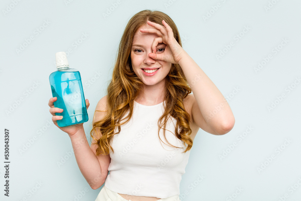 Young caucasian woman holding a mouthwash isolated on blue background excited keeping ok gesture on eye. Young caucasian woman holding a mouthwash isolated on blue background excited keeping ok gesture on eye.