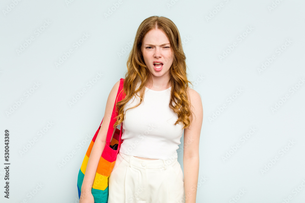 Young caucasian woman holding LGTBI bag isolated on blue background screaming very angry and aggressive. Young caucasian woman holding LGTBI bag isolated on blue background screaming very angry and aggressive.