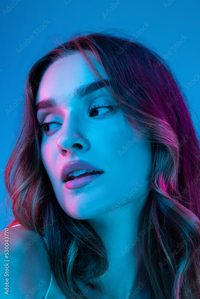 Portrait of young beautiful girl with curly long hair posing isolated over blue blackground in neon. Looks calm and relaxed. Closeup Portrait of young beautiful girl with curly long hair posing isolated over blue blackground in neon. Looks calm and relaxed. Closeup