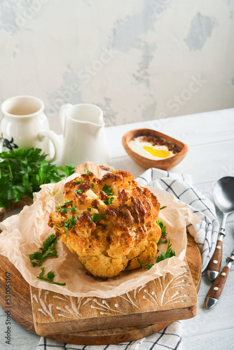Baked cauliflower. Oven or whole baked cauliflower spices and herbs server on wooden rustic board on old white wooden background table. Delicious cauliflower. Eyal Shani dish. Perfect tasty snack. photo