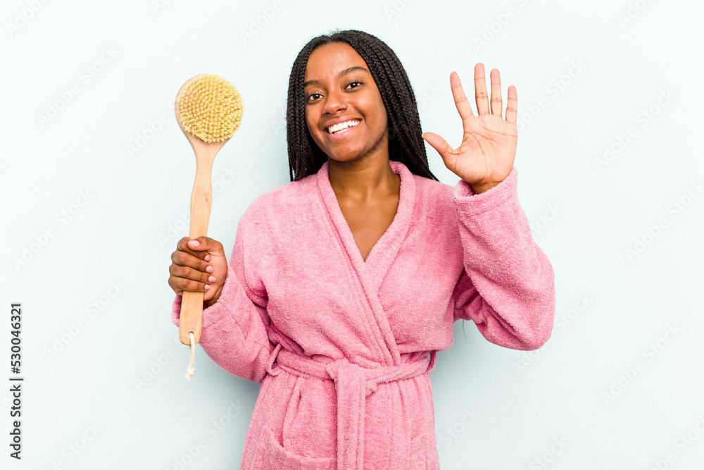 Young African American woman holding a bathtub brush isolated on blue background smiling cheerful showing number five with fingers. Young African American woman holding a bathtub brush isolated on blue background smiling cheerful showing number five with fingers.