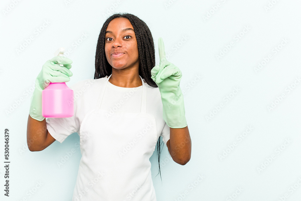Young African American cleaner woman isolated on blue background showing number one with finger. Young African American cleaner woman isolated on blue background showing number one with finger.