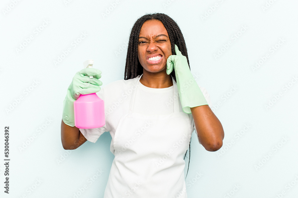 Young African American cleaner woman isolated on blue background covering ears with hands. Young African American cleaner woman isolated on blue background covering ears with hands.