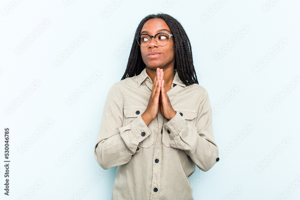 Young African American woman with braids hair isolated on blue background praying, showing devotion, religious person looking for divine inspiration. Young African American woman with braids hair isolated on blue background praying, showing devotion, religious person looking for divine inspiration.