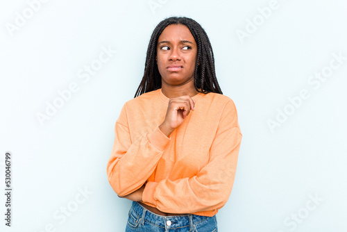 Young African American woman with braids hair isolated on blue background confused, feels doubtful and unsure.