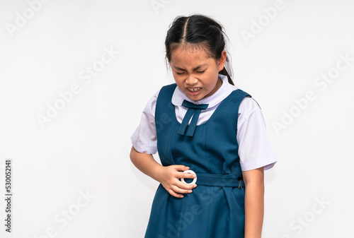 Little Asian student girl is stomach ache, unidentified school uniform, isolated portrait of Asian child girl with stomach pain on white background. photo