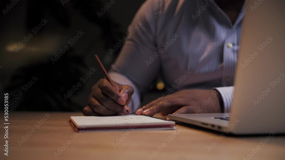 African man doing online learning at home.Business person work remotely using laptop.Black male writing on notepad doing distance education on computer African man doing online learning at home.Business person work remotely using laptop.Black male writing on notepad doing distance education on computer