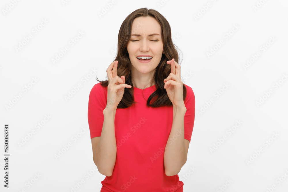 portrait of smiling brunette woman with closed eyes and with fingers crossed, she makes wish in red T-shirt on white background for advertising, copy space, template portrait of smiling brunette woman with closed eyes and with fingers crossed, she makes wish in red T-shirt on white background for advertising, copy space, template