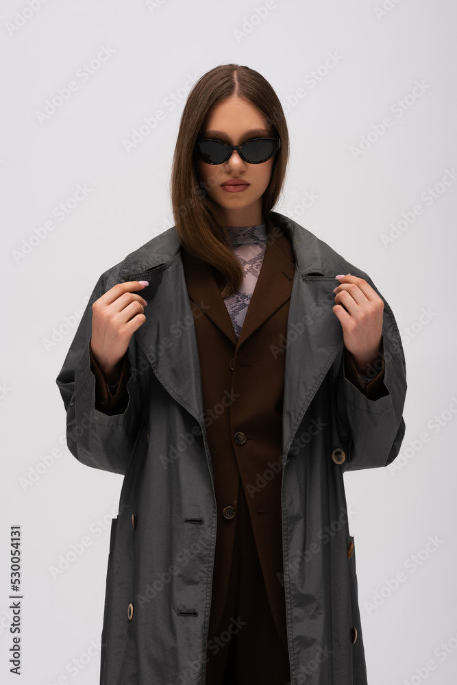 stylish teenage girl in sunglasses and trendy trench coat posing isolated on grey.