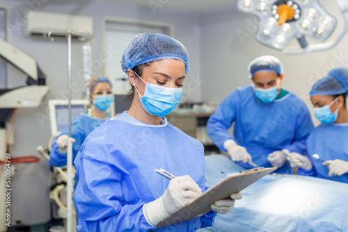 Surgeon writing on clipboard in operation room, anaesthesiologist writing the updates