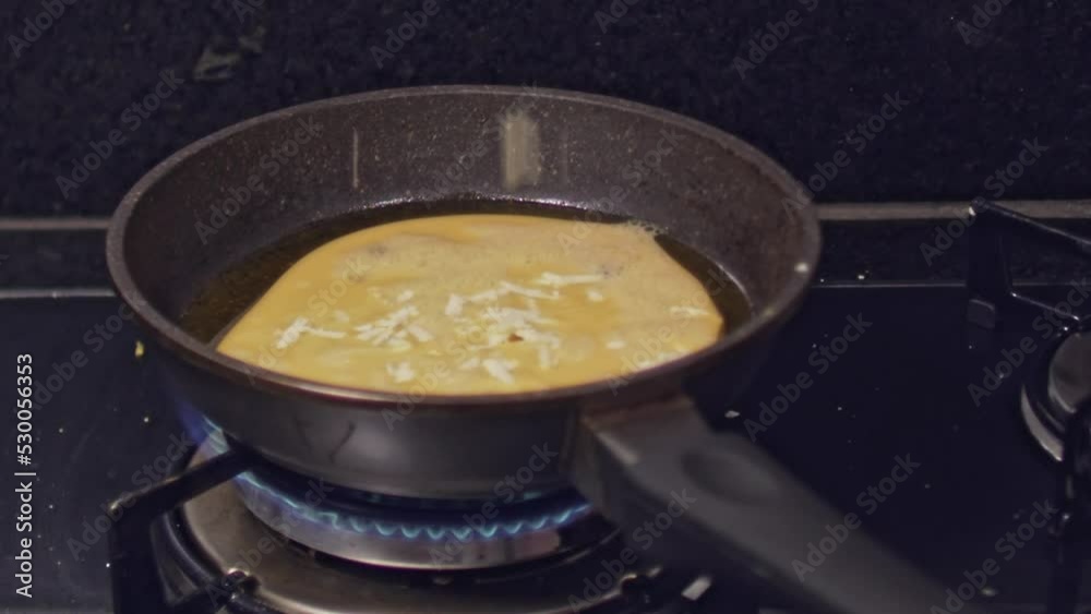 Slow motion, sprinkling cheese onto omelet frying in a pan at home kitchen Slow motion, sprinkling cheese onto omelet frying in a pan at home kitchen