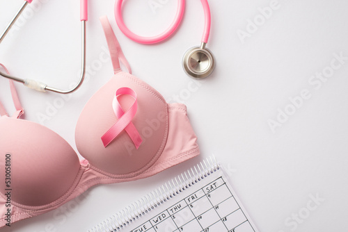 Breast cancer awareness concept. Top view photo of pink brassiere with pink ribbon stethoscope and calendar on isolated white background