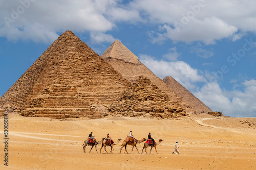 Cairo, Egypt. 08.25.2022. Group of tourists riding camels seeing the pyramids of Menkaure, Chephren and Cheops.