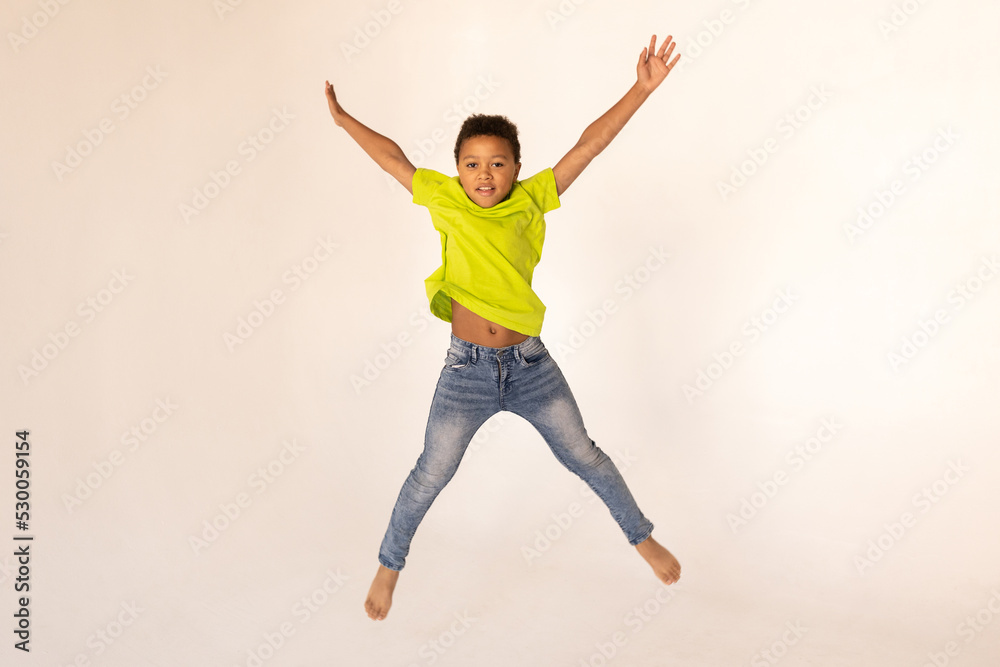 Portrait of happy preteen boy jumping against white background. Excited mixed race child wearing green T-shirt and jeans having fun. Happiness concept