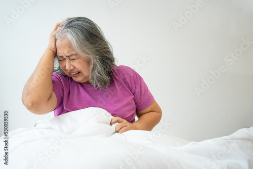 Unhealthy elderly senior Asian woman sitting on bed suffering from headache and migraine so pain and illness, Stress senior woman sit on bed at home alone, tried, Unhappy Elderly despond concept